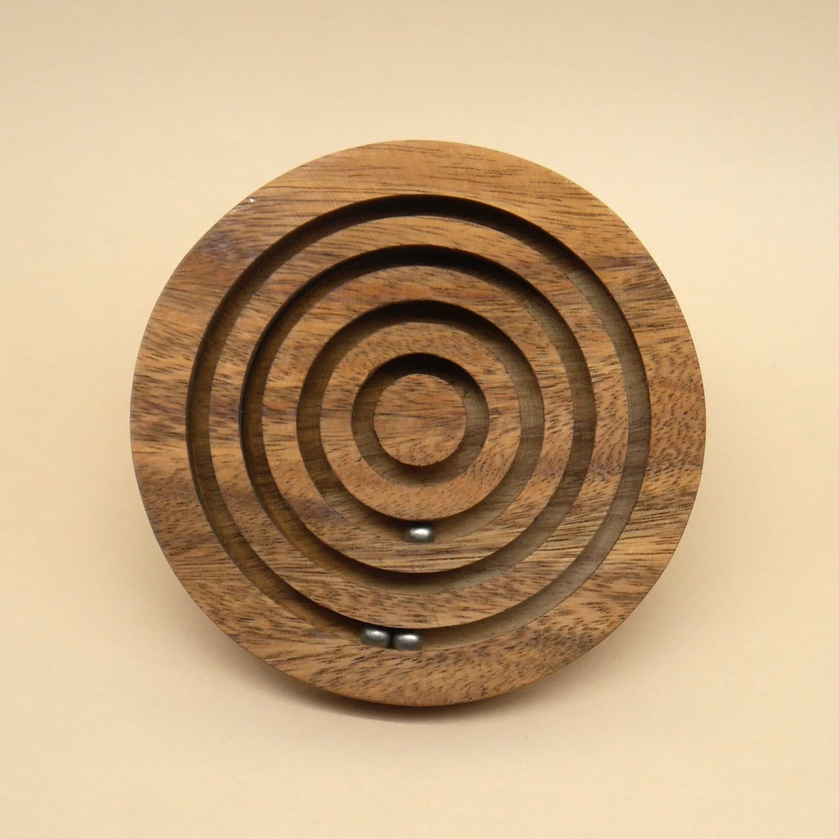 Frontale Ansicht eines runden Holz‑Geduldspiel‑Labyrinths mit konzentrischen Rillen; zwei kleine Stahlkugeln ruhen im unteren Bereich.