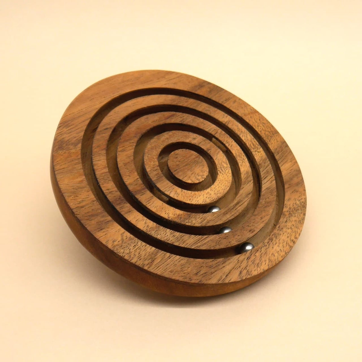 Seitlich geneigtes Holz‑Labyrinth mit fünf ringförmigen Spuren; zwei Stahlkugeln rollen in den inneren Ringen.