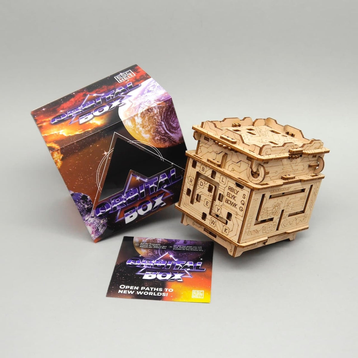 Holz-Schatztruhe „Orbital Box“ mit Rätselmechanik neben Verpackung – ein cleveres Denkspiel für kreative Köpfe.