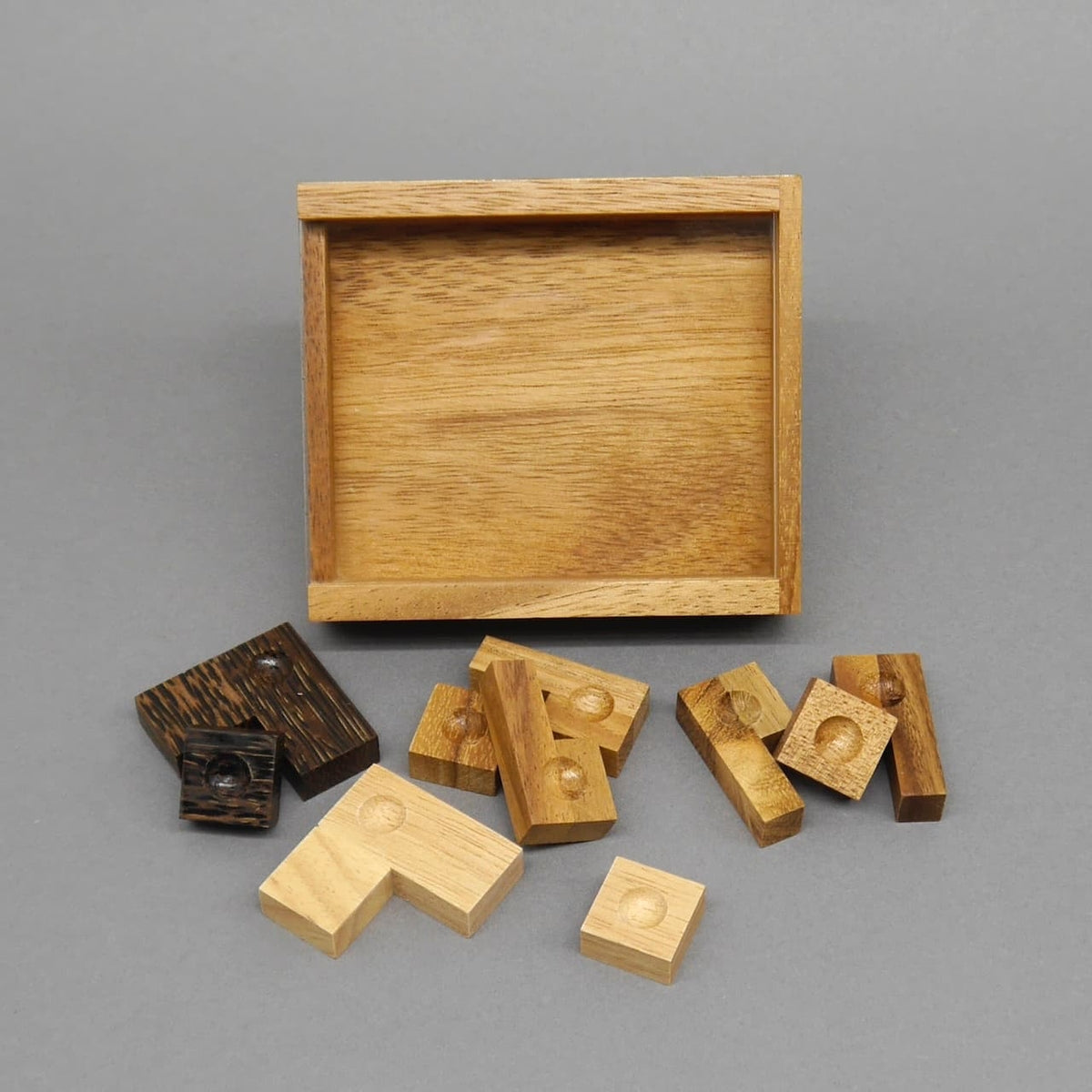 Leere, rechteckige Holzbox und verstreute, gelochte Spielsteine eines kniffligen Holzspiel.