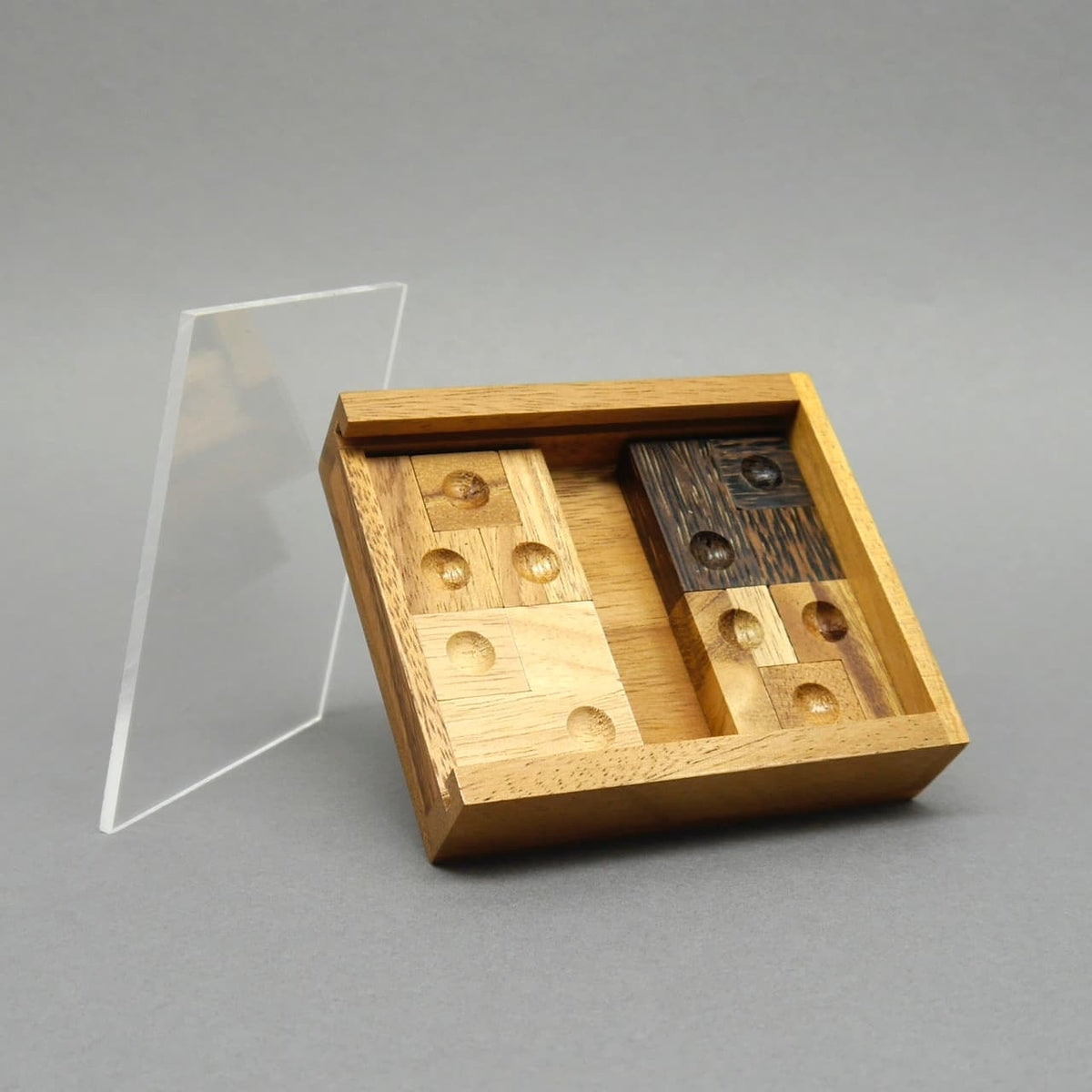 Teilweise gelöstes Sliding‑Puzzle in einer schräg stehenden Holzschale; gelochte Steine ordentlich angeordnet.