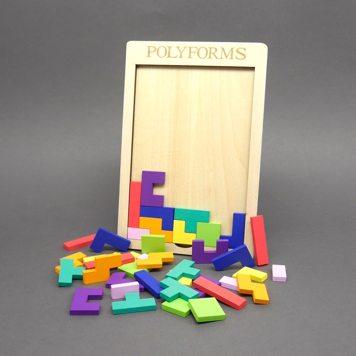 Ein leerer Holzrahmen mit dem Schriftzug „POLYFORMS“, vor dem zahlreiche bunte Puzzleteile verstreut auf dem grauen Untergrund liegen. Einige Teile befinden sich noch im unteren Bereich des Rahmens.