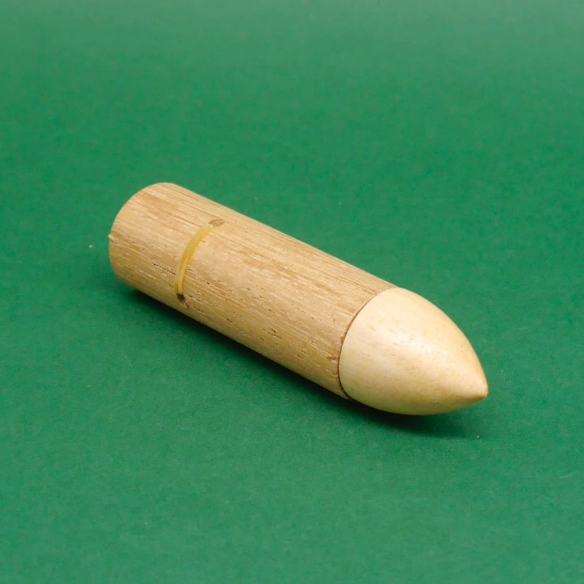 Holz‑Schnapper Trick, Joke‑Geduldspiel: fertig zusammengesetztes Magic‑Trick‑Spiel, raketenförmig und glatt zulaufend auf grünem Grund.
