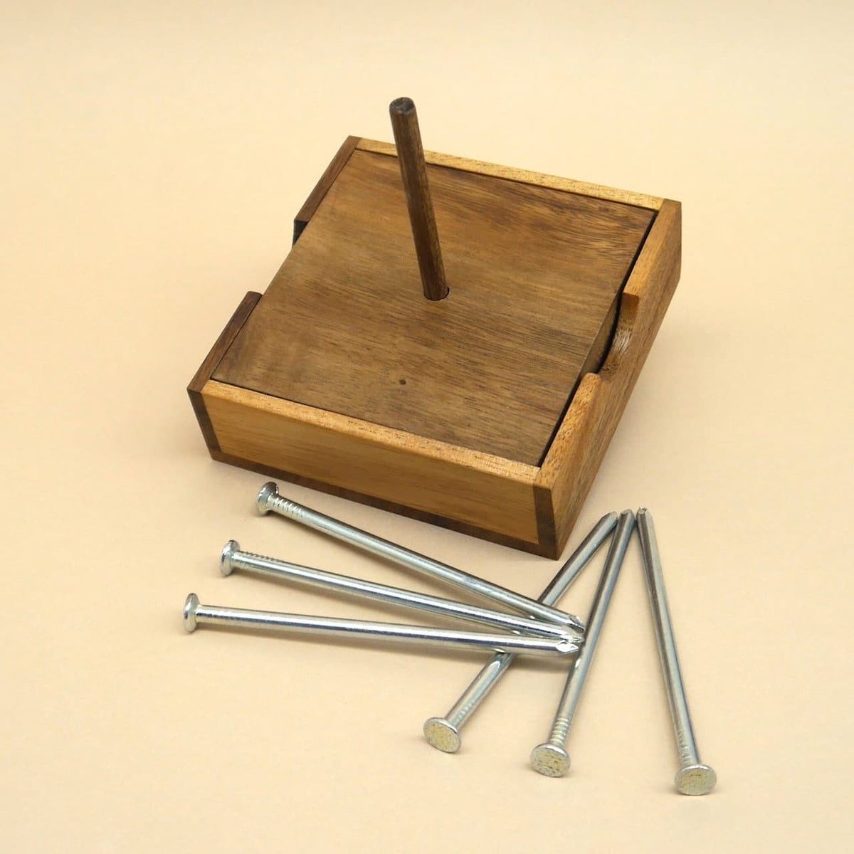 Holzbox mit mittigem Stab und sechs blanken Nägeln auf hellem Untergrund – minimalistisches Denkspiel zum Ausbalancieren.