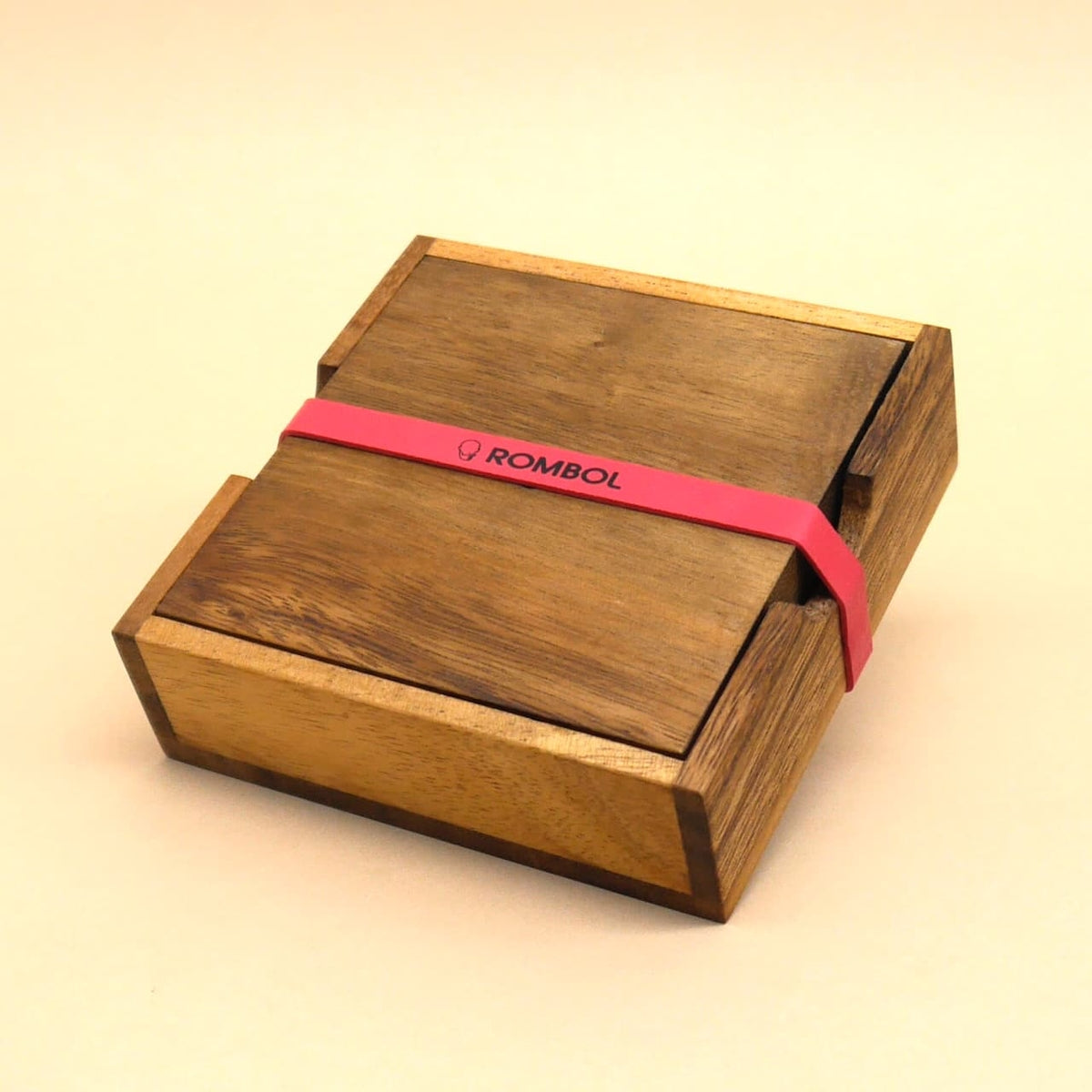 Quadratische Holzbox von Rombol, mit rotem Gummiband verschlossen – stilvolles Geschicklichkeitsspiel als Geschenk.