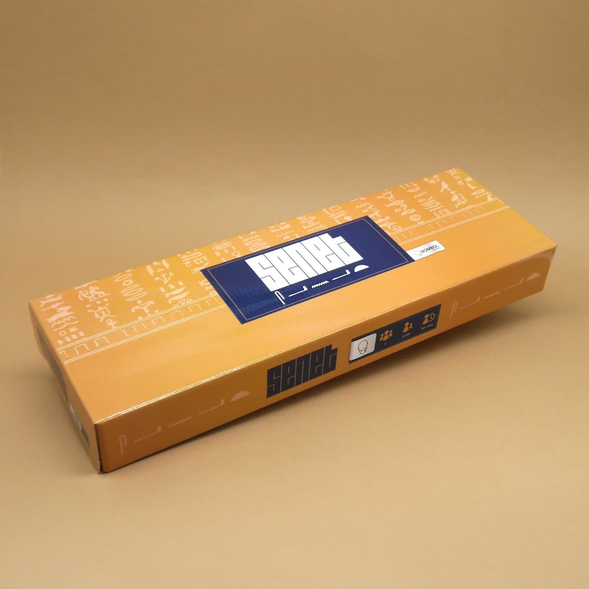 Schmale Verpackung des Senet Holzspiels in warmem Ocker mit weißen Hieroglyphen und blauem Logo auf neutralem Hintergrund.