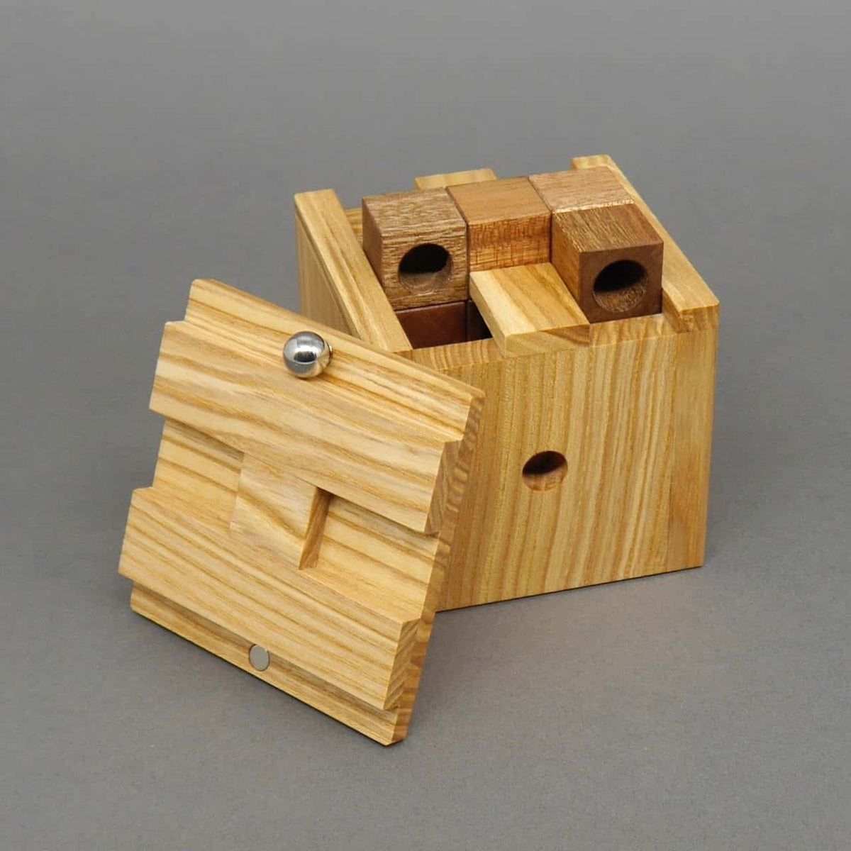 Teilweise geöffneter Holz-Würfel mit eingesetzten Puzzle-Elementen, daneben liegt der abgenommene Deckel mit Metallkugel.