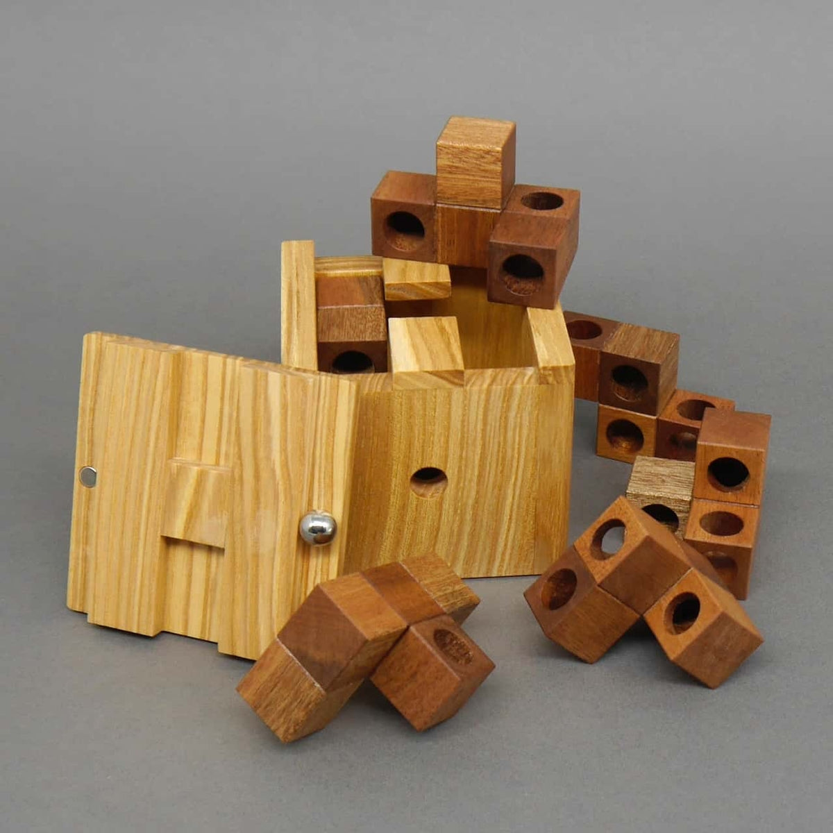 Holzbox mit geöffnetem Deckel und verstreuten Puzzleteilen drumherum – ein komplexes Holz-Denkspiel.