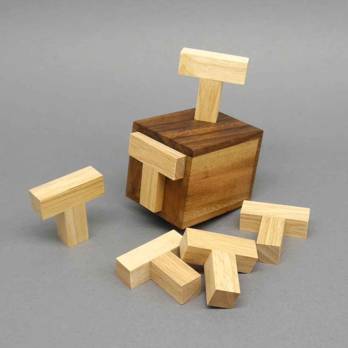 Mehrere T-förmige Holzsteine stecken und lehnen an einer aufrecht stehenden, braunen Holzbox; weitere liegen davor – Veranschaulichung des Puzzles im Spiel.
