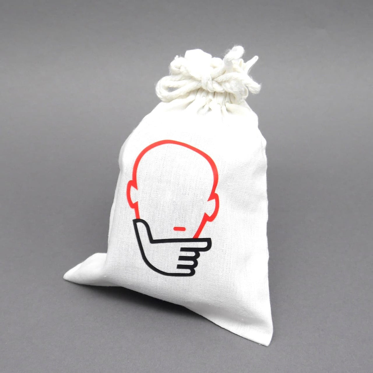 Weißer Stoffbeutel mit Kordelzug und stilisiertem Denker-Logo (Kopf und nachdenkliche Hand) auf grauem Hintergrund – Verpackung des „Six T“-Puzzles
