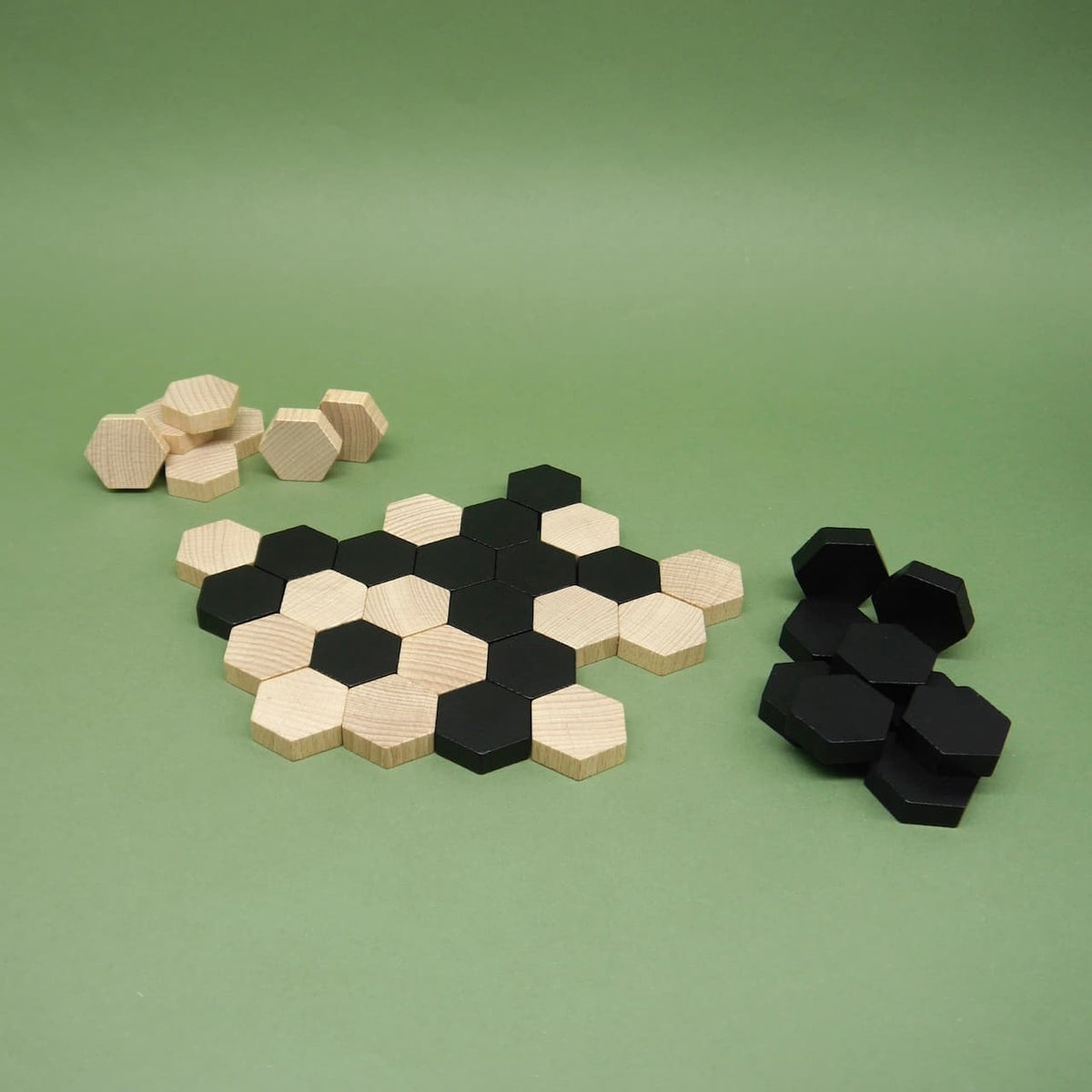 Aufgebaute Steine des lernspiel „SIX“: schwarze und helle Holzhexagone formen ein Muster, Reststapel liegen seitlich.