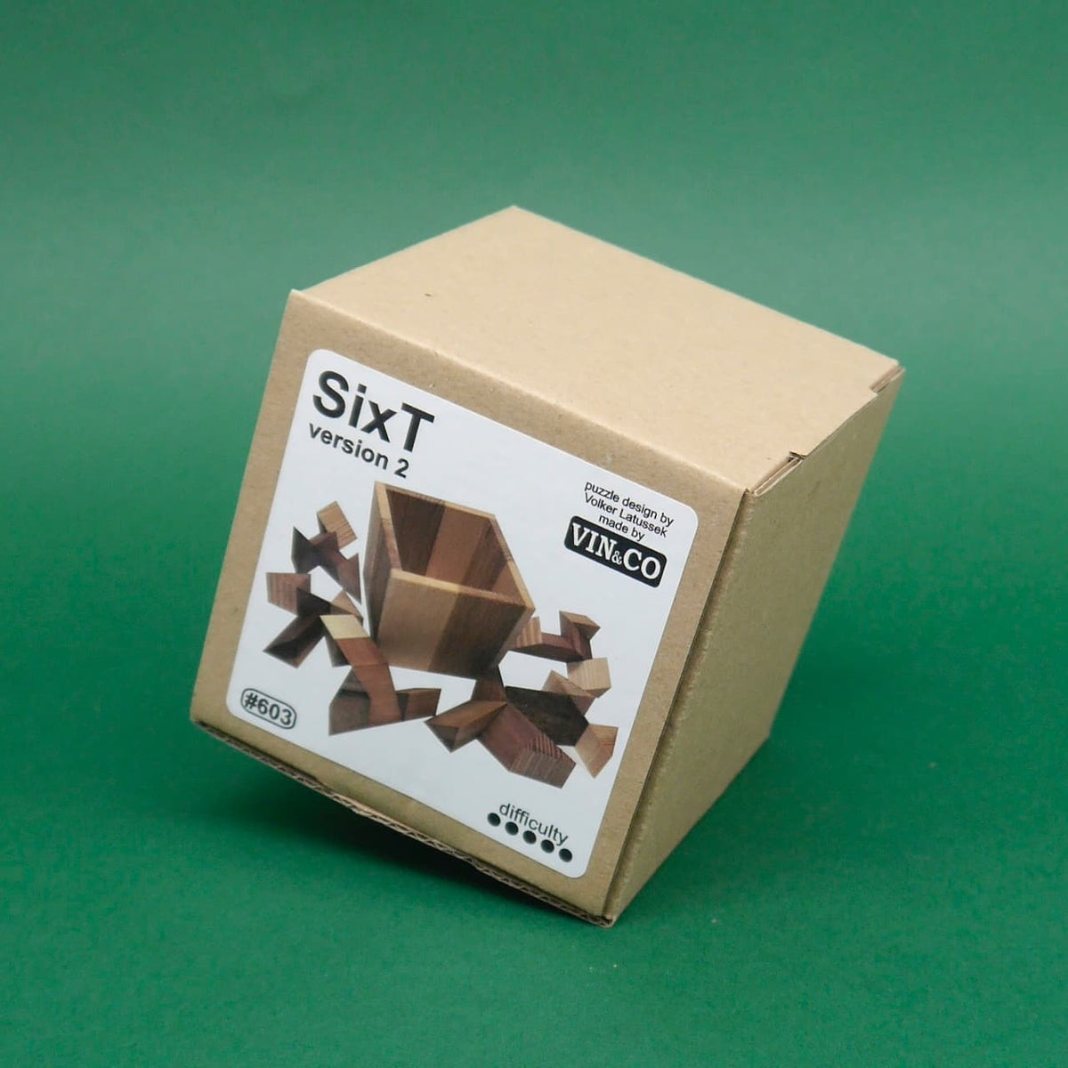 Knobelbox SixT Version 2: Holzpuzzle im Karton mit Produktlabel vor grünem Hintergrund.