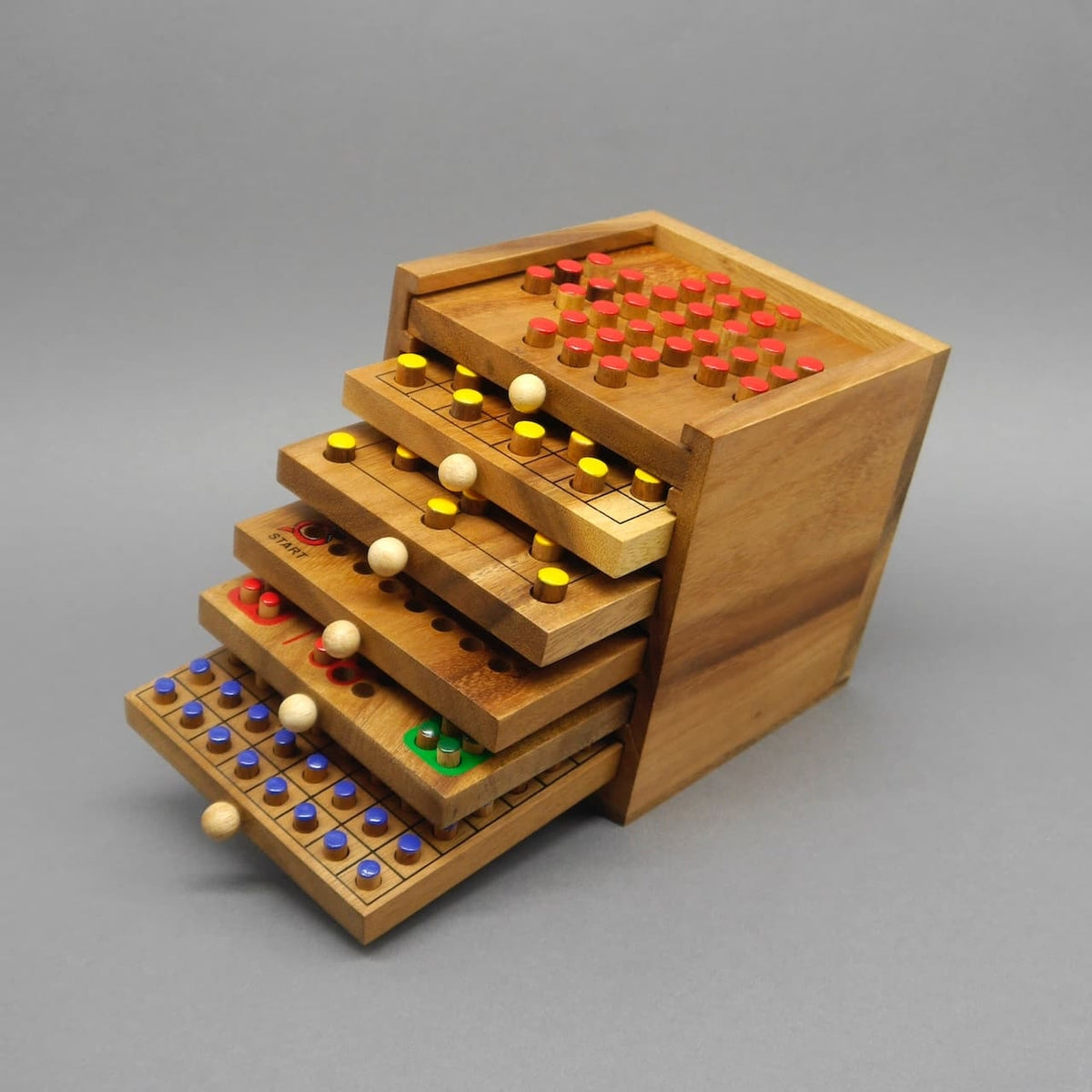 Offene Holzbox mit ausgezogenen Brettspiel-Schubladen und bunten Stecksteinen – vielseitige Holzspiele für knobelige Runden.
