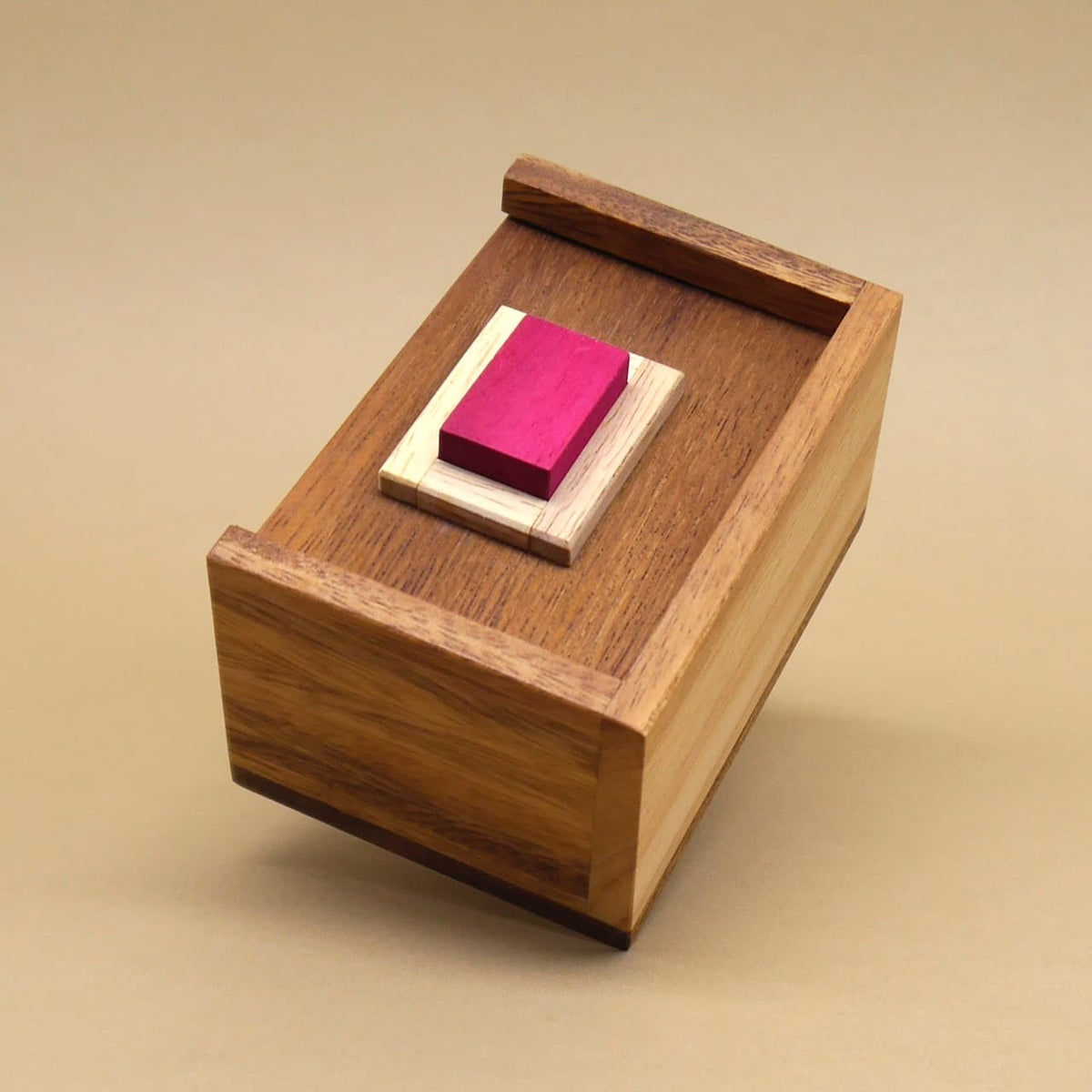 Geschlossene Teufelstein-Holzbox mit erhöhtem Podest und leuchtend rotem Stein als Denkspiel auf schlichtem beigem Hintergrund.