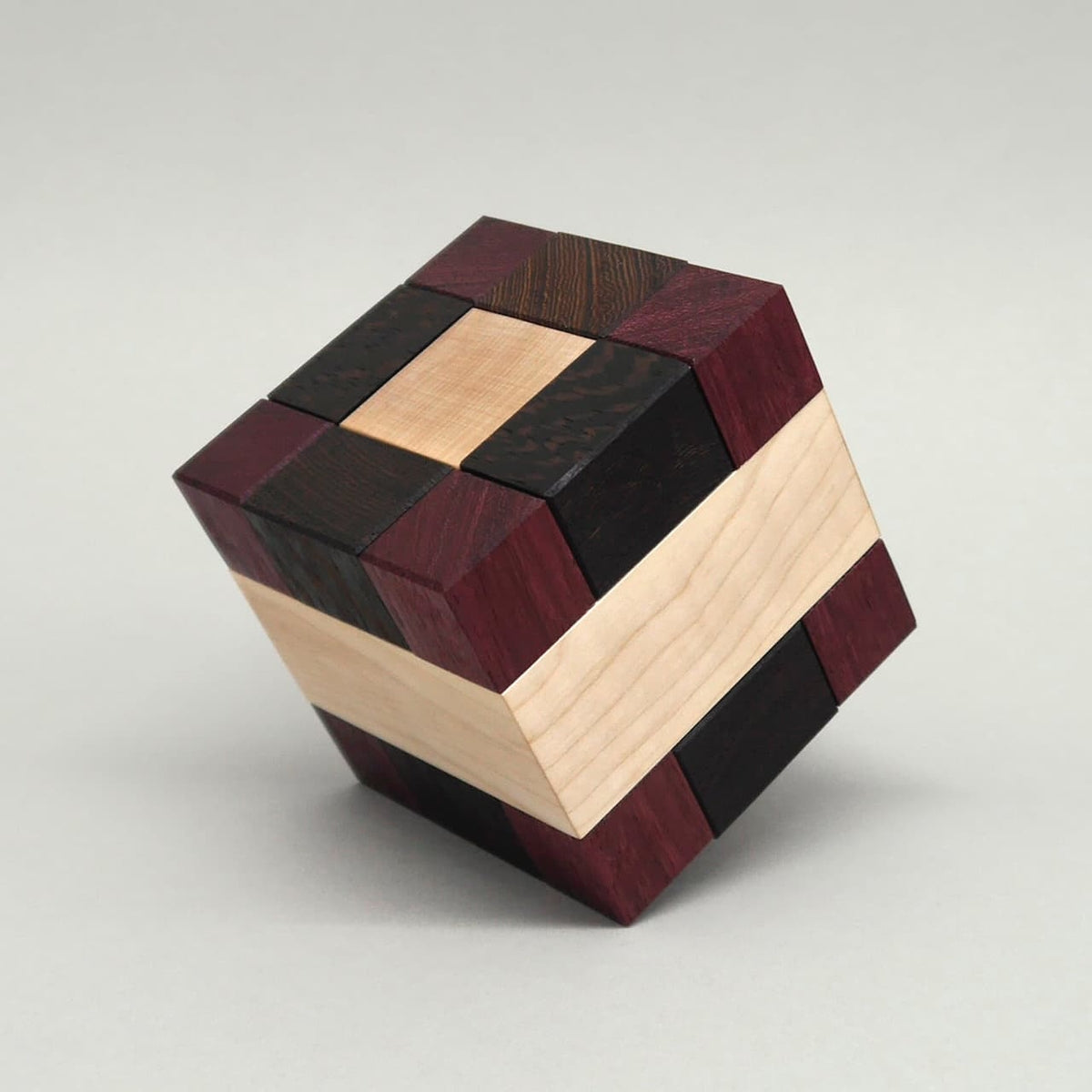 Knobelspiel in Form eines Holzpuzzles aus dunklen, rötlichen und hellen Holzblöcken, perfekt zu einem Würfel gefügt.
