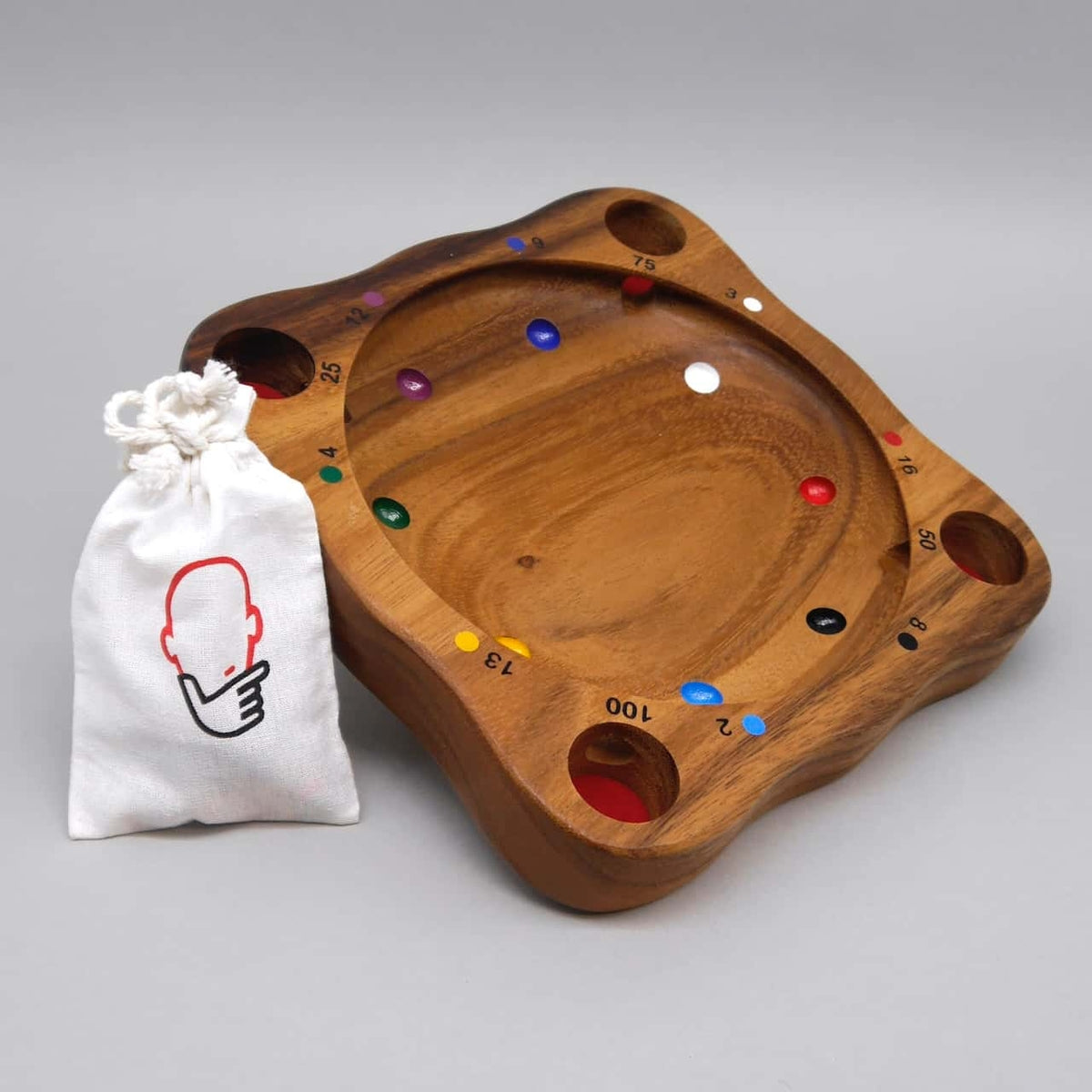 Holzbrett „Tiroler Roulette“ mit bunten Punkt-Markierungen und vier Vertiefungen, daneben ein kleiner Stoffbeutel – traditionelles Brettspiel für gesellige Runden.