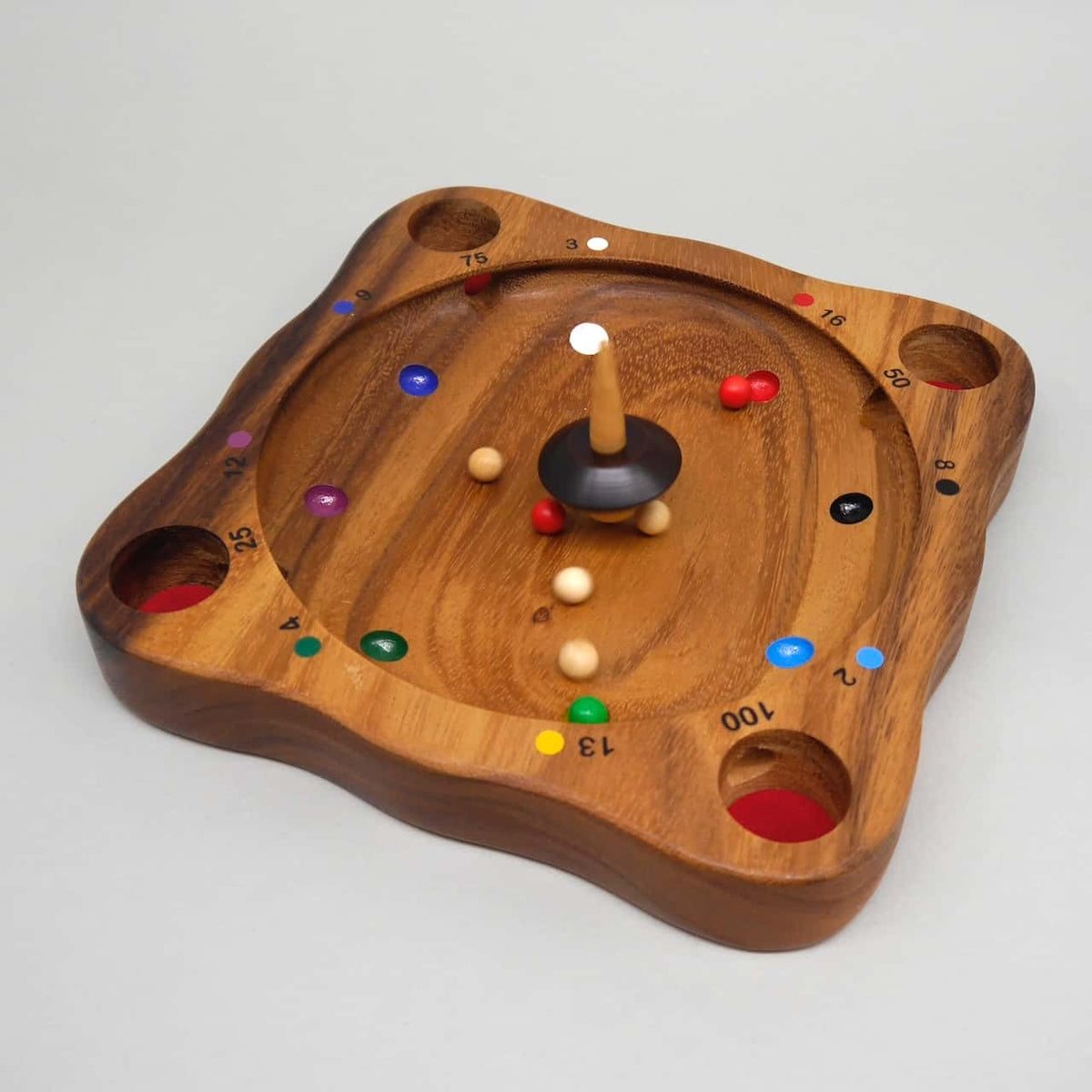 Ein Kreisel wirbelt mitten auf dem „Tiroler Roulette“-Brett, während farbige Kugeln über nummerierte Felder rollen – klassisches Kreisel-Geschicklichkeitsspiel aus Holz.