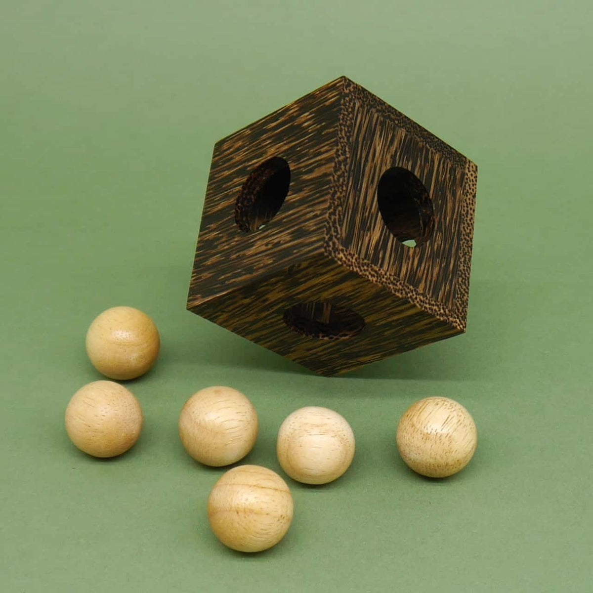 Dunkler Holzwürfel mit runden Öffnungen und sechs hellen Holzkugeln davor – ein herausforderndes Denkspiel für Puzzle-Fans