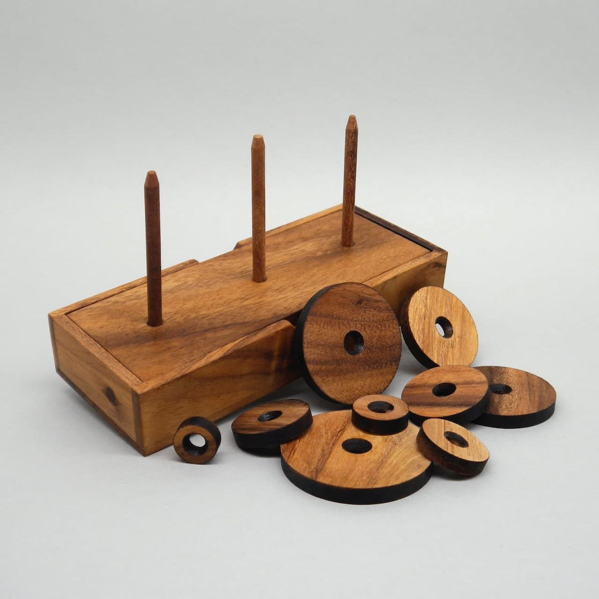 Zerlegter Turm von Hanoi als Knobelspiel mit Holzscheiben vor der Basis mit drei Stäben.