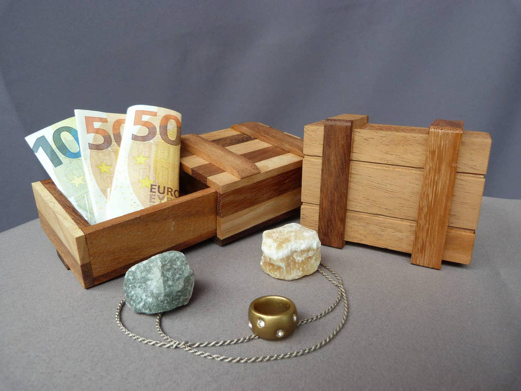 Holzkästchen mit Euro-Geldscheinen, daneben zwei Steine, ein goldfarbener Ring und eine Silberkette