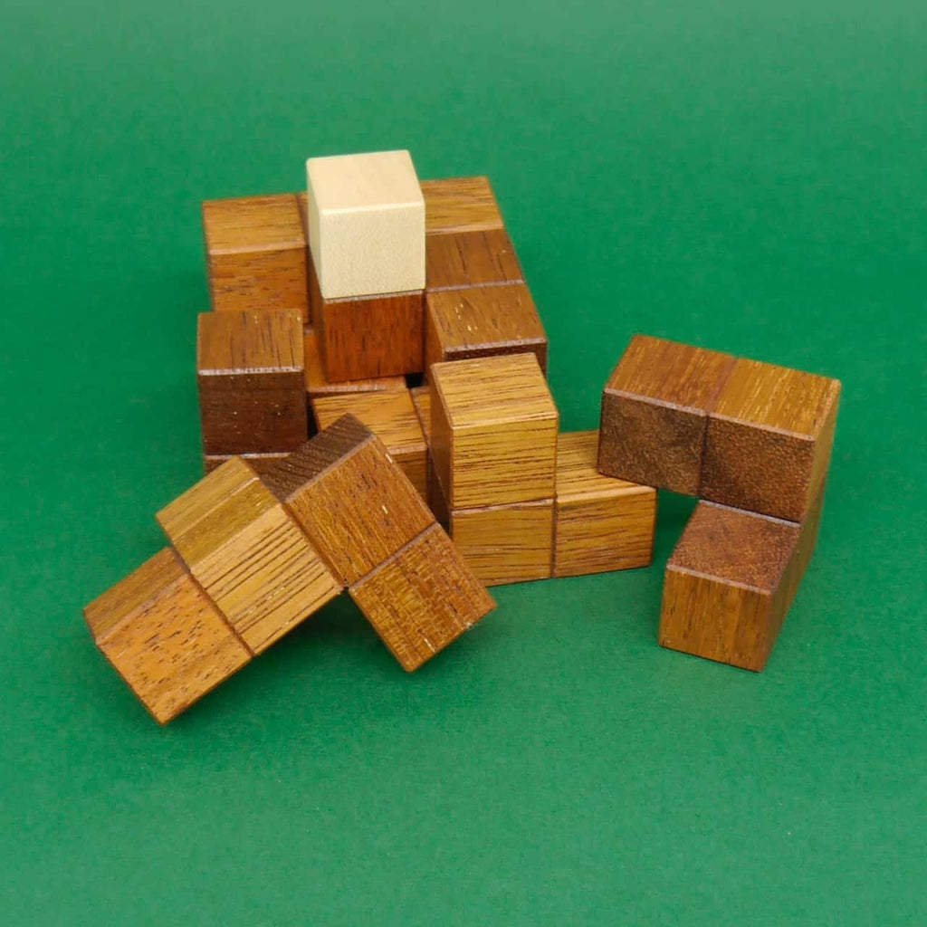 Puzzle aus Holz: lose Würfelmodule eines 3D-Denkspiels liegen auf grünem Filz verteilt.