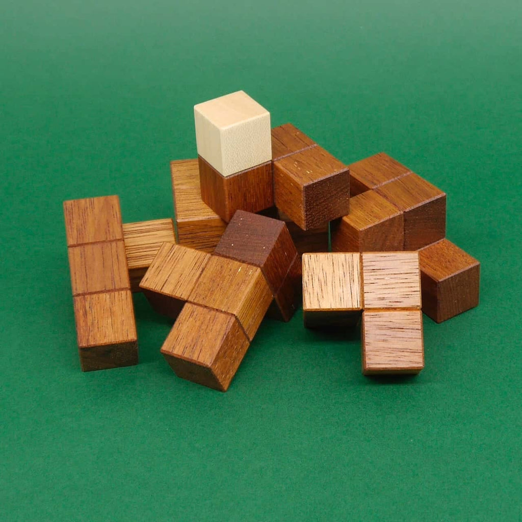 Zerlegter SomaCube: unterschiedlich geformte Holzbausteine des klassischen Denkspiels sind vor grünem Hintergrund verstreut.