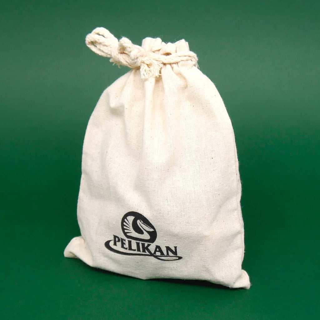 Geduldsspiel im Stoffbeutel: naturfarbener Baumwollsack mit Pelikan-Logo, oben zugeknotet, steht vor einem grünen Hintergrund.