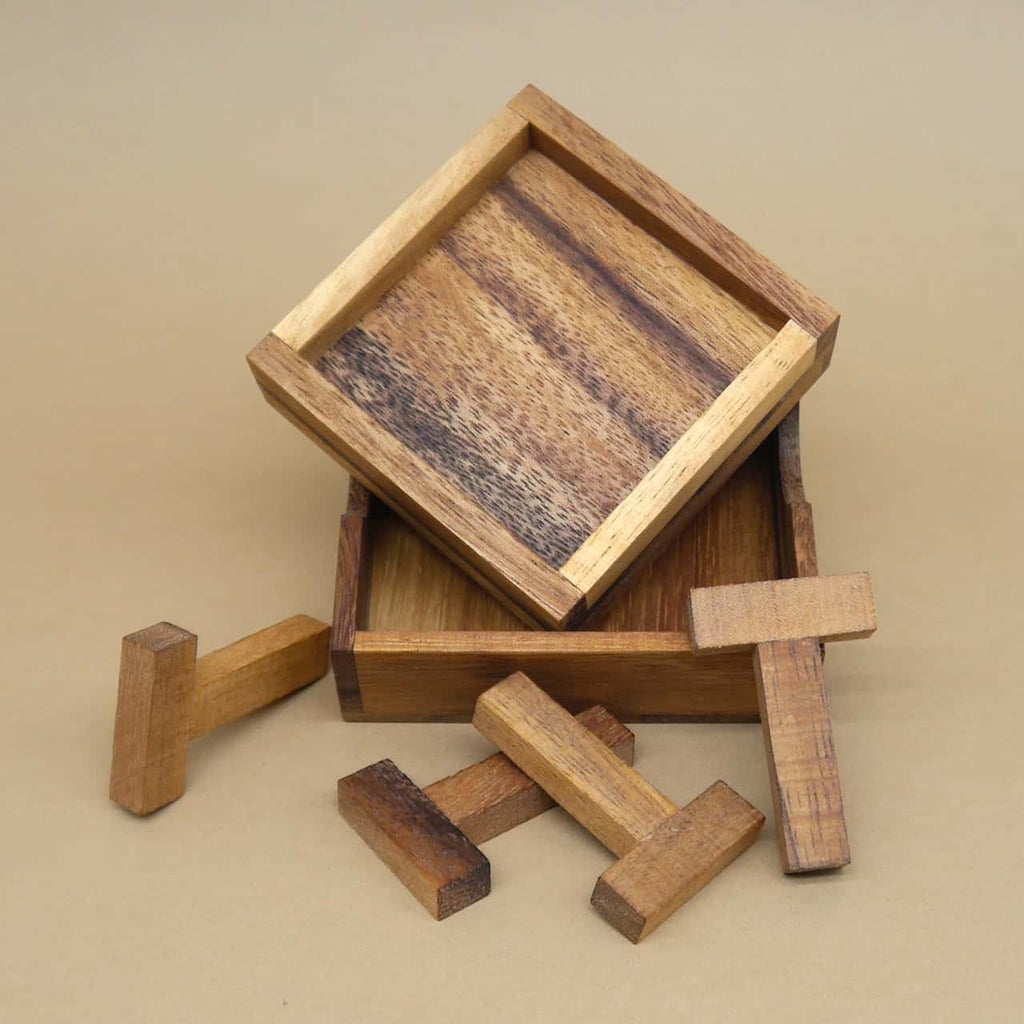 Zerlegtes Logikpuzzle aus Holz: Deckel liegt schräg auf der Box, lose T-Steine davor.