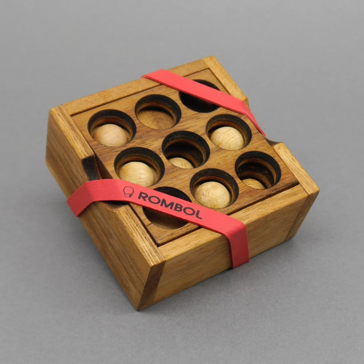 Quadratische Holzbox mit neun runden Vertiefungen und teils eingesetzten Kugeln – Geduldsspiel in geschlossenem Zustand.