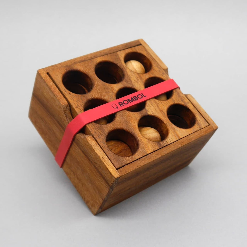 Quadratisches Holzpuzzle „9 Loch“ in geschlossener Box; die gelochte Deckplatte ist mit einem roten Band fixiert.