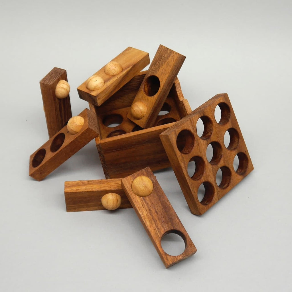 Zerlegte Holzstücke des 9‑Loch‑Puzzles liegen vor der Box verstreut und laden zum Gehirntraining ein.