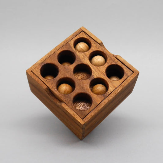 Vollständig montiertes 9‑Loch‑Knobelspiel; alle Holzkugeln sitzen exakt in den runden Vertiefungen der Box.