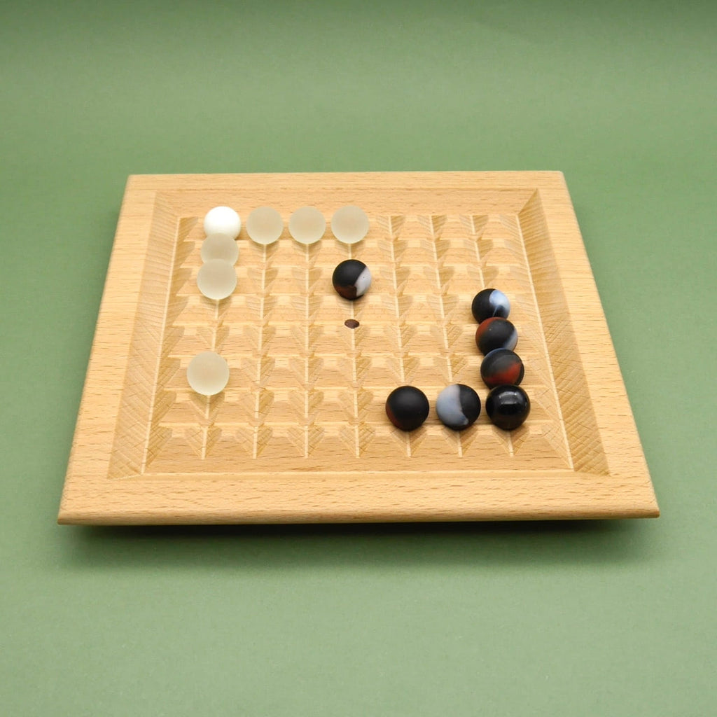 Quadratisches Spielfeld mit gefrästen Rillen und hellen/dunklen Kugeln rund um das Zentrum des Bretts – Murmelspiel.