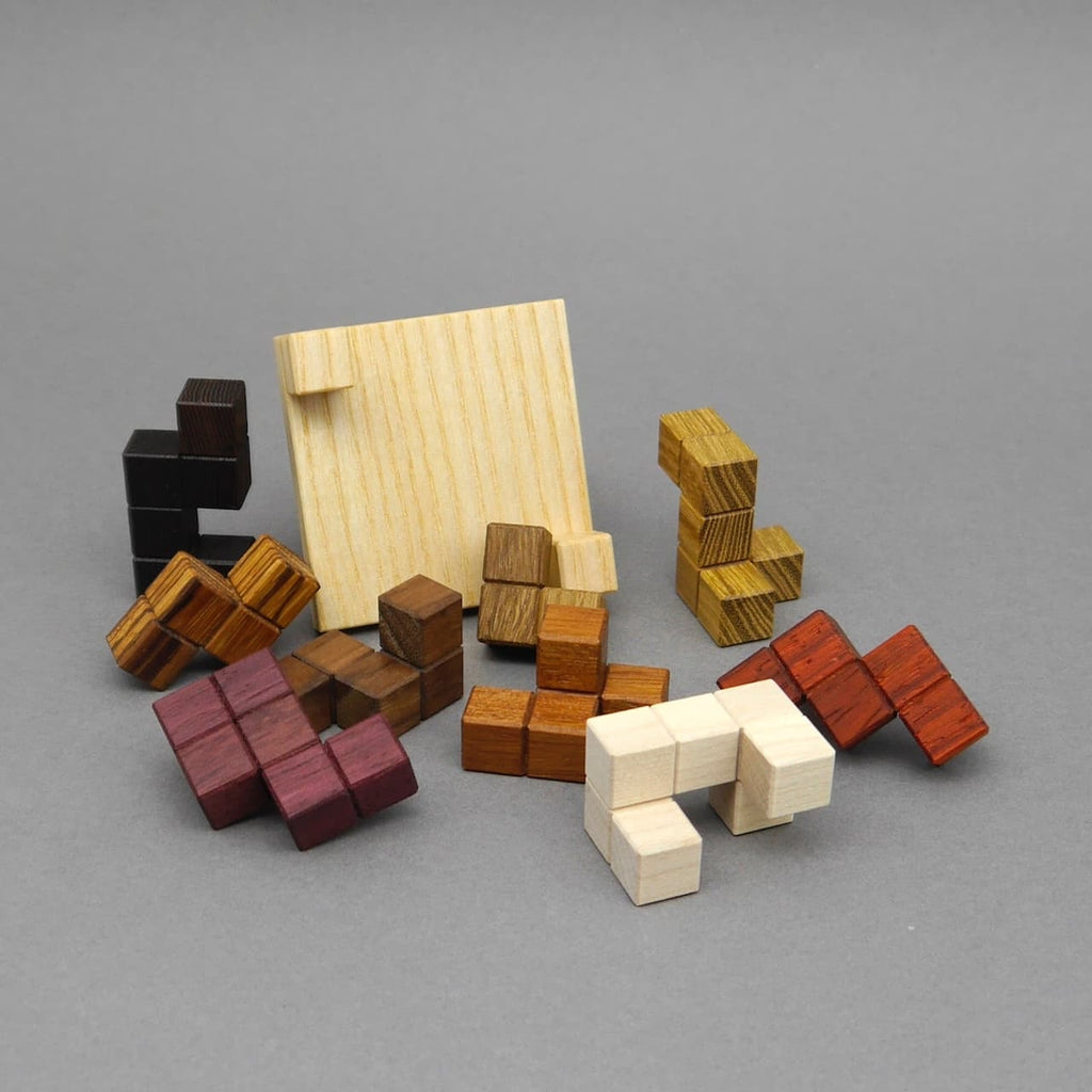 Auseinandergelegtes Knobelspiel mit Holzbausteinen und rechteckigem Rahmen auf grauem Untergrund.