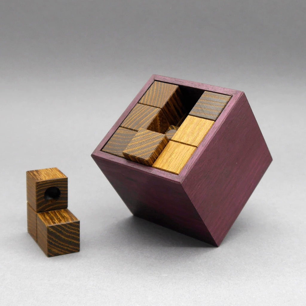 Lila lackierte Puzzlebox „Apteek“ zum Gehirntraining: im geöffneten Würfel liegen Holzteile, daneben ein einzelnes Teil mit Bohrung.