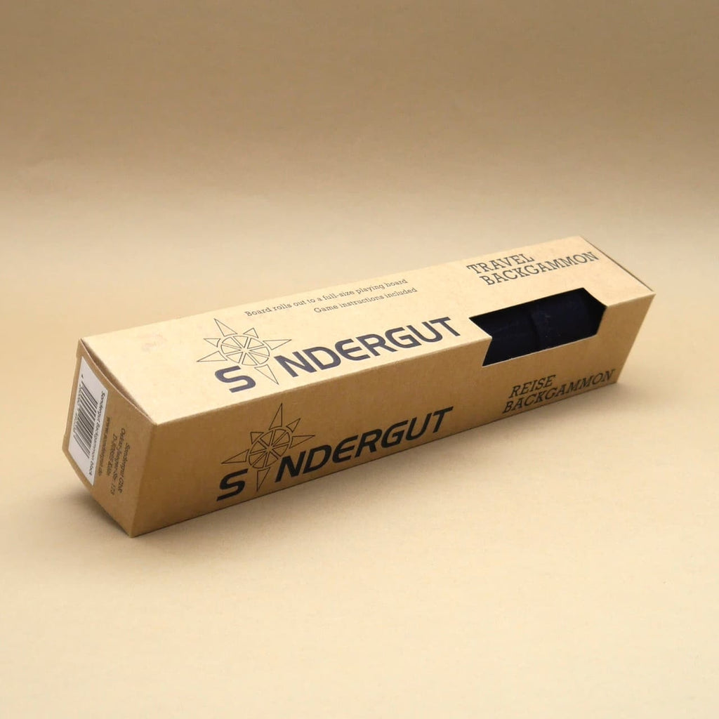 Backgammon-Set: längliche Kartonverpackung mit Sichtfenster, Marke Sondergut, Reiseversion, fotografiert vor beigem Hintergrund.
