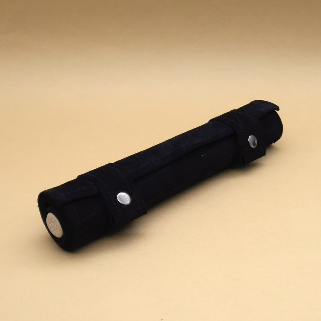 Backgammon: zusammengerolltes schwarzes Reisebrett in weicher Ledertasche mit Druckknöpfen, freigestellt vor beigem Hintergrund.