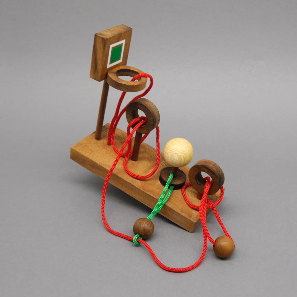 Ein kniffliges Seilpuzzle aus Holz mit Basketballkorb-Optik und farbigen Schnüren zur Förderung der Problemlösefähigkeit.