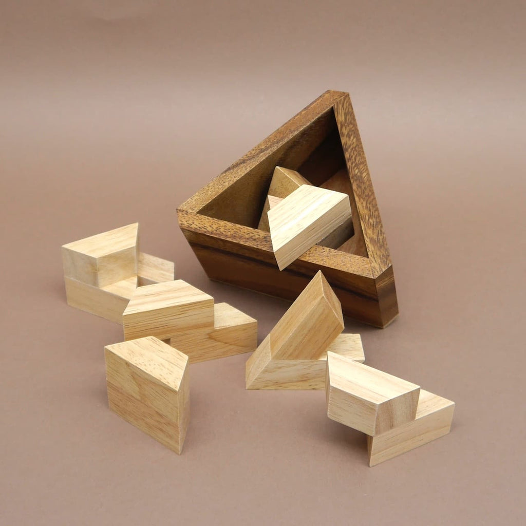 Mehrere helle Bausteine eines Bermuda-Dreieck Holzpuzzles schweben vor der kantigen Dreieckschatulle aus Holz.