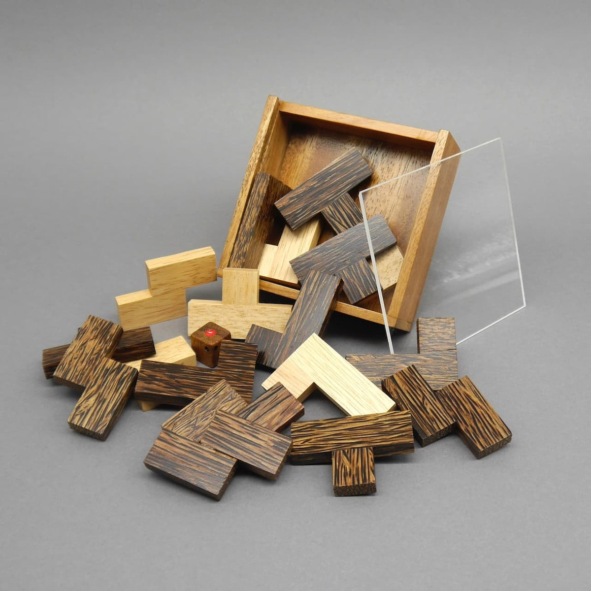 Kippende Holzbox verstreut L‑förmige Steine, Würfel und Acryldeckel – dynamische Momentaufnahme eines Taktikspiel.