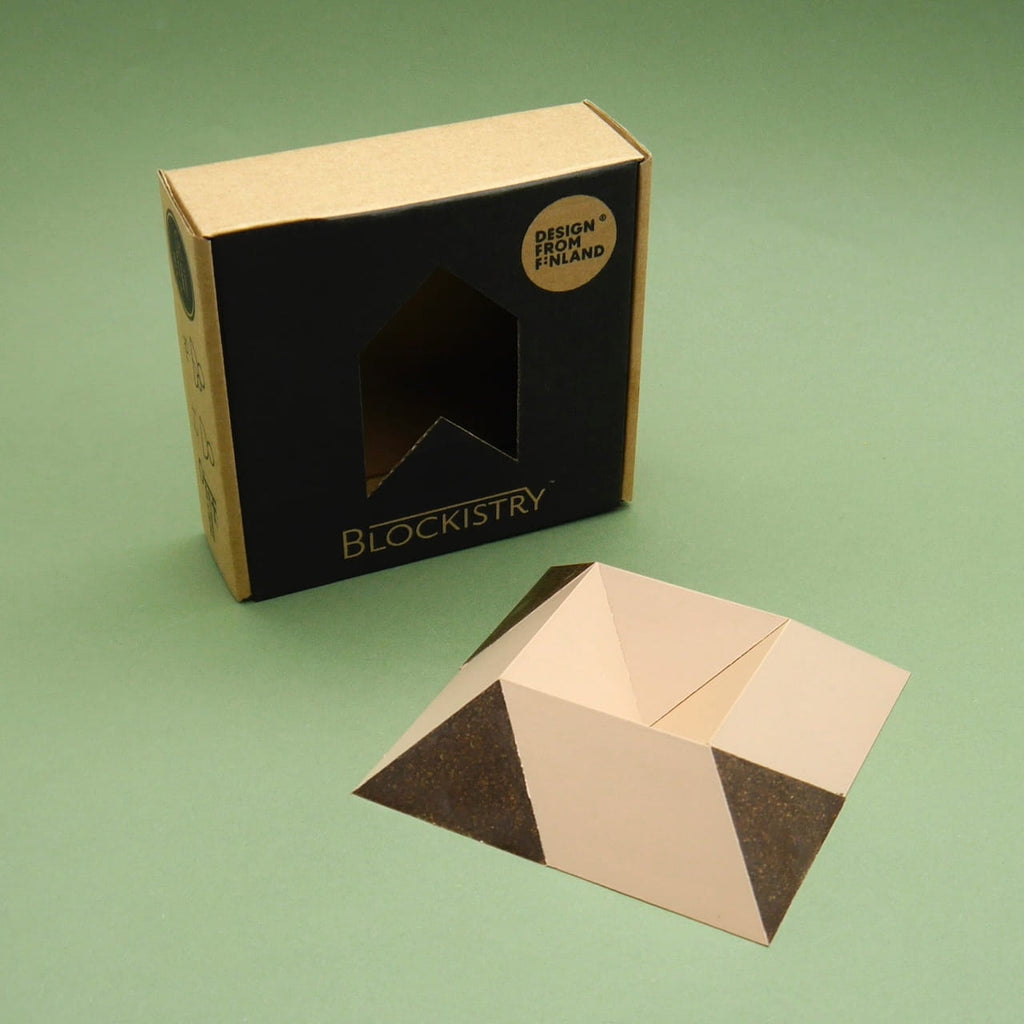 Blockistry Denkspiel 3D Puzzle zeigt Verpackung und gefaltete Pyramidenform aus Karton, minimalistisches Design vor grünem Hintergrund.