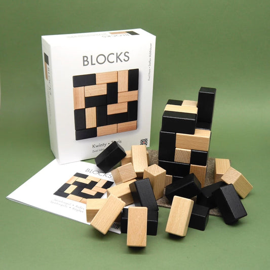Blocks-Stapelspiel aus Holz mit Bausteinen in Schwarz und Natur, aufgebaut neben Verpackung und Anleitung.