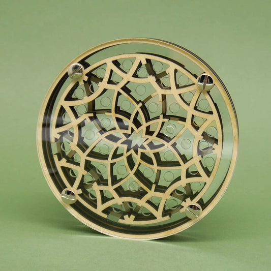 Frontalansicht eines aufrecht stehenden, kreisförmigen Holz-Acryl-Labyrinths mit sternförmigem Blütenornament und vier Schraubköpfen vor schlichtem, grünem Hintergrund.