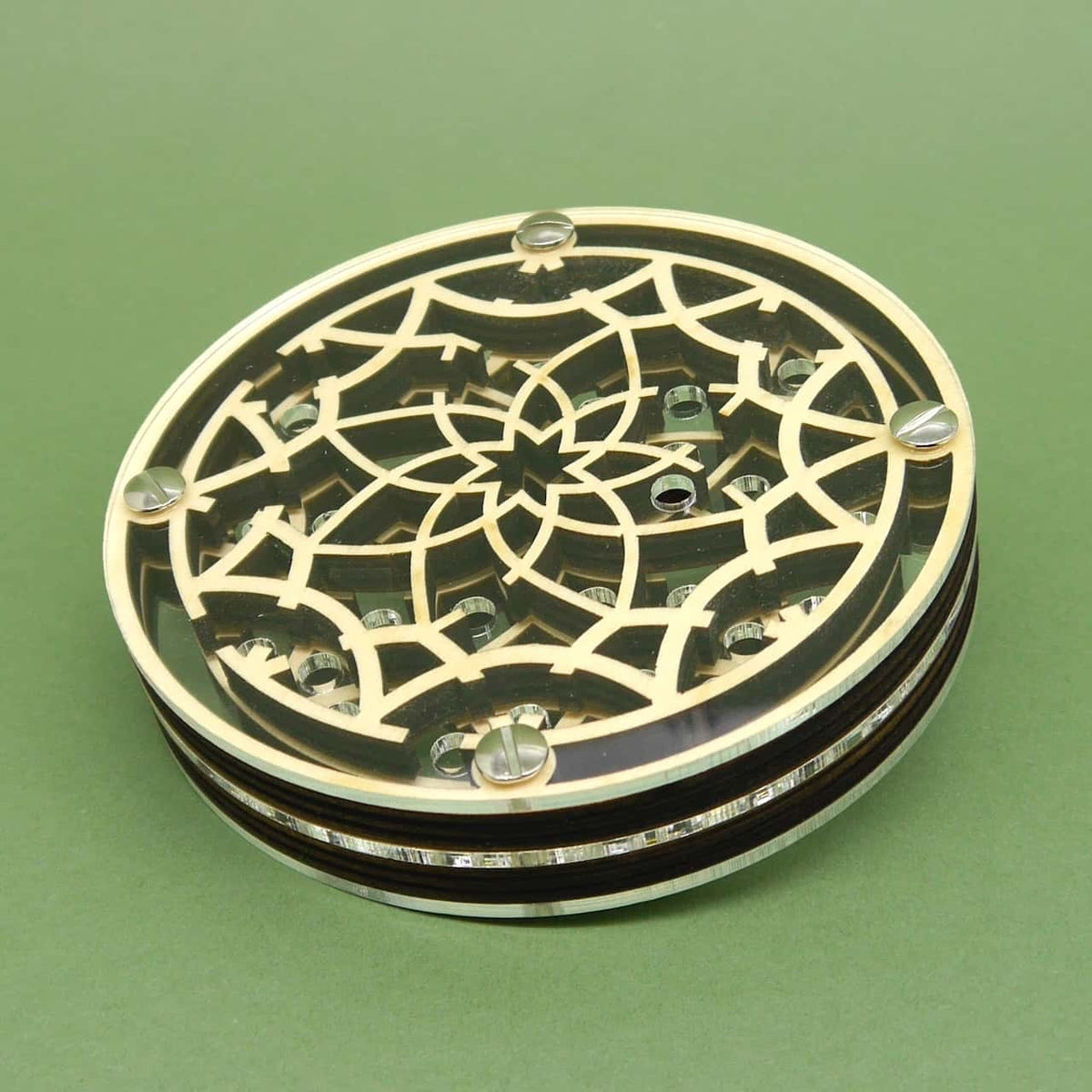 Schräg liegende Perspektive auf das mehrlagige Kugellabyrinth; transparente Acrylscheibe offenbart ein helles, florales Holzgeflecht mit Metallkugeln, gehalten von vier Schrauben, auf grünem Untergrund.