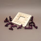  Offenes Holzrahmen-Puzzle „Broken Frame and Window“ mit verstreuten lila Holzsteinen als Geduldspiel.