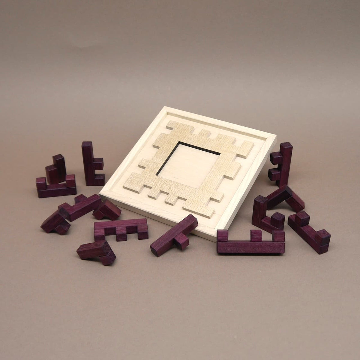  Offenes Holzrahmen-Puzzle „Broken Frame and Window“ mit verstreuten lila Holzsteinen als Geduldspiel.
