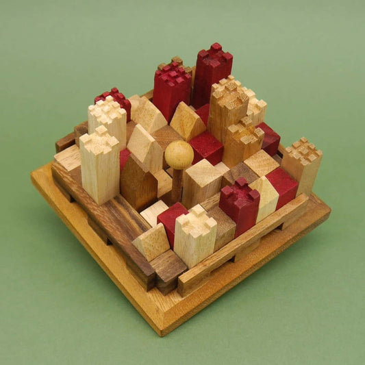 Holzbausteine in Rot- und Naturtönen bilden ein kompaktes 3D-Puzzle in Burgform, dicht an dicht auf einem quadratischen Holzbrett vor grünem Hintergrund angeordnet.
