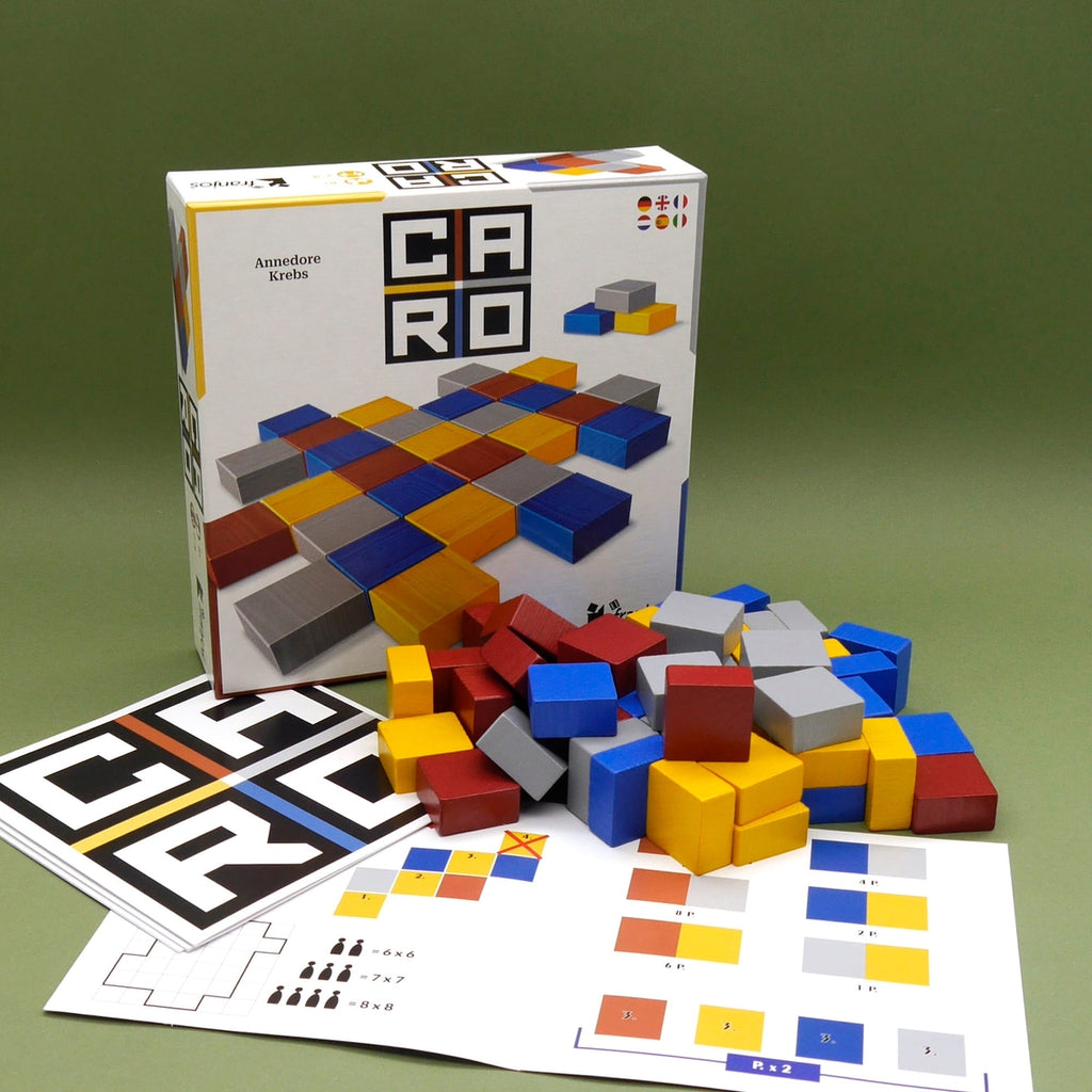 Familienspiel CARO mit bunten Holzklötzen, Spielkarten und Verpackung auf grünem Hintergrund arrangiert.