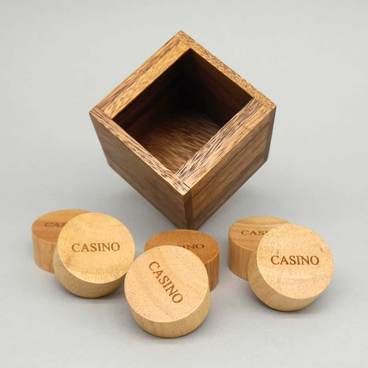 Casino-Packingpuzzle: leerer Holzwürfel und verstreute Rundsteine als anspruchsvolles Geduldsspiel-Rätsel.