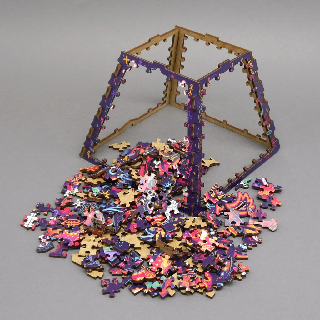 Aufgestellte Rahmen einer pyramidenförmigen Knobelbox mit verstreuten, bunt bedruckten Holzpuzzle-Teilen auf grauem Hintergrund.